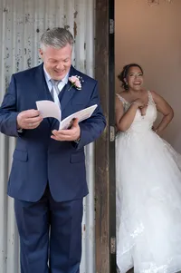 Bride laughs in the doorway as groom looks though an intimate portrait album she gifted his before their wedding ceremony.
