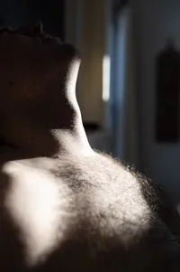 Close-up of a non-binary persons chest and neck as a small glimpse of light hits them.