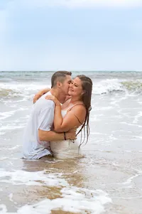 Man kissing his fiancé's neck in the ocean.