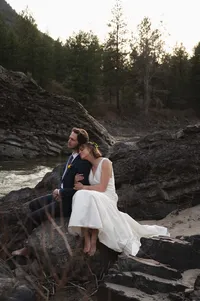 Newlyweds sitting together on rocks beside a river after their Montana elopement.