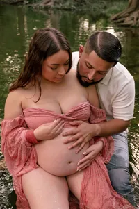 Expecting parents sitting in a creek and examining mom's pregnant belly.