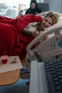Expectant mother smiles at the camera while eating Jell-O in her hospital bed before her baby’s birth.