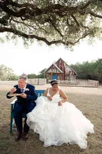 Groom eats food next to his bride as she examines her dress.