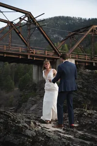 Bride smiling at her groom as she leads him up a hill near a bridge.