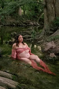 Expecting mother relaxes in a creek while holding her bump.