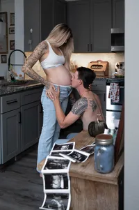 Husband kisses his wife's baby bump in the kitchen as the sonogram photos sit in the foreground.