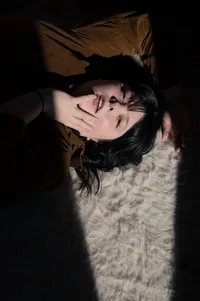 Woman Laying on the floor in a sliver of light as she look into the camera sensually.