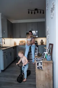 Expectant parents embrace as their toddler rides his bike around the apartment.