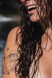 Close-up of a woman's tattoo as she smile with wet hair.