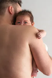 A Newborn Peeks Over Their Father’s Shoulder.
