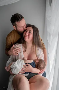 Postpartum parents embracing each other as their baby breastfeeds.