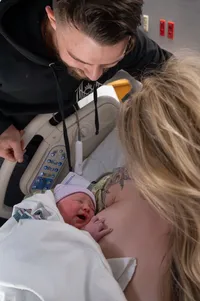 Parents admire their newborn as mom holds her against her chest.