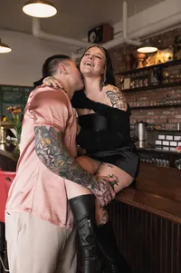 A tatted up couple playfully kissing on a bar top.