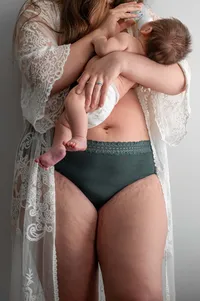 Woman holds her baby in her arms as the camera focuses on her stretchmarks in a beautiful way.