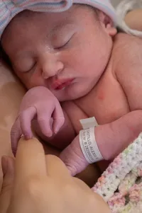 Close-up of a newborn baby sleeping and holding her mother's finger.