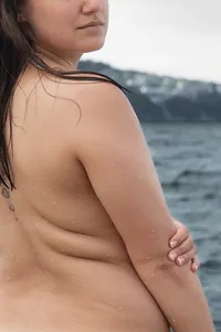Close-up of a queer woman's back, showing her rolls in a beautiful light.