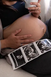 Expecting mother sips coffee as the camera focuses on the sonogram photos on her lap.