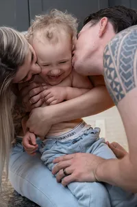 Expecting parents attacking their toddler with kisses and love.