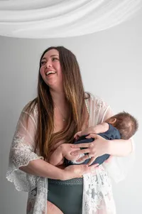 Postpartum mom holding her baby and smiling off camera.