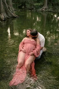 Expectant parents rest in a creek as Mom leans on Dad’s chest.