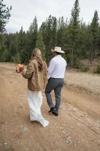 Bride and groom walk down a path hand-in-hand as she wears his jacket over her dress during their elopement.