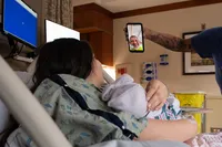 Postpartum mother introduces her newborn during a video call from her hospital bed.