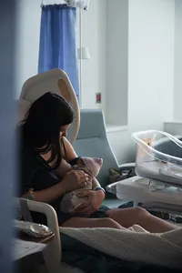 New mother breastfeeds her baby in a quiet, softly lit hospital room.