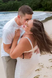 An Engaged couple playfully embracing each other and laughing on the beach.