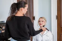 Bride getting soft glam bridal makeup with a red lip and a romantic updo with loose face framing pieces by The Bridal Glam Group