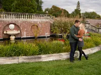 An engaged couple kisses beside a brick garden fountain and reflecting pool.