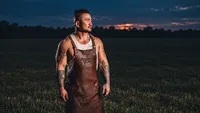 Stephen Kina of 406 BBQ wearing a leather apron outdoors at dusk