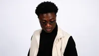 Maxjuice wearing glasses and a cream vest against a white background