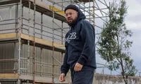 Robinhood Regz wearing a dark hoodie beside a scaffolded building