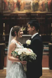 Bride and groom smiling at each other in front of the painted mural above the altar, her bouquet between them