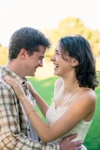 Engaged couple laughing face to face in soft golden light, her hand resting on his shoulder