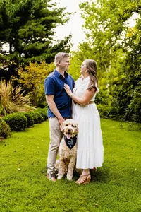 Brittany and Ben standing together on a garden lawn with their goldendoodle sitting at their feet