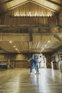 Mike and Molly dancing together in the middle of a large empty wooden barn with a vaulted ceiling
