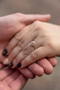Close-up of a sparkling halo engagement ring on her hand resting in his