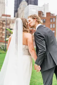 Groom leaning in to kiss his bride on a city lawn as her long veil falls down her back