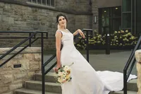 Hannah in her wedding gown posing on the stone steps of the church beside an iron railing