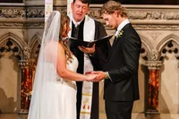 Bride and groom holding hands at a carved stone altar as the officiant reads during their church ceremony