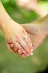 Close-up of her hand holding his, showing her new engagement ring