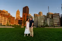 Rebecca and Jordan standing on a wide lawn at sunset with the downtown Pittsburgh skyline glowing behind them