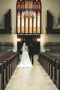 Bride and groom at the end of the aisle beneath the tall stained glass window at Church of the Ascension
