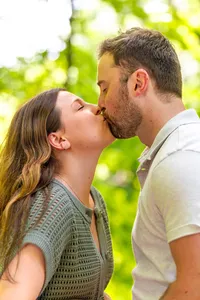 Newly engaged couple kissing among green trees