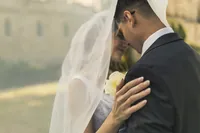 Bride resting her hand on the groom's shoulder as they lean in close beneath her veil, cream flowers between them