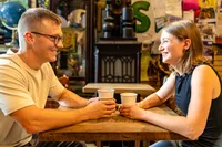 Couple laughing across a wooden table over two coffees in a cozy, colorful cafe