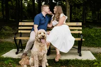 Brittany and Ben on a park bench with their goldendoodle sitting in front of them