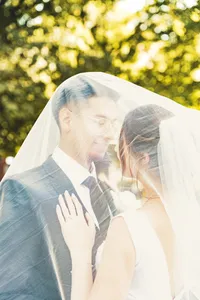 Bride and groom sharing a quiet moment under her veil with sunlit green leaves behind them