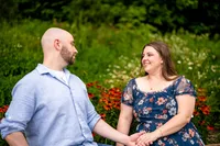 Kathy and Ben sitting in the grass holding hands in front of red flowers and white wildflowers